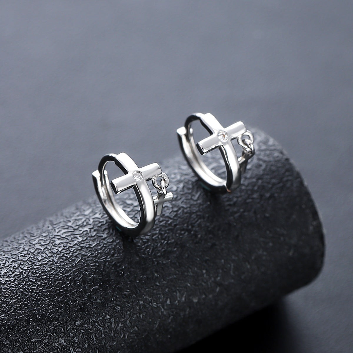 Silver cross hoops with zircon on textured black surface