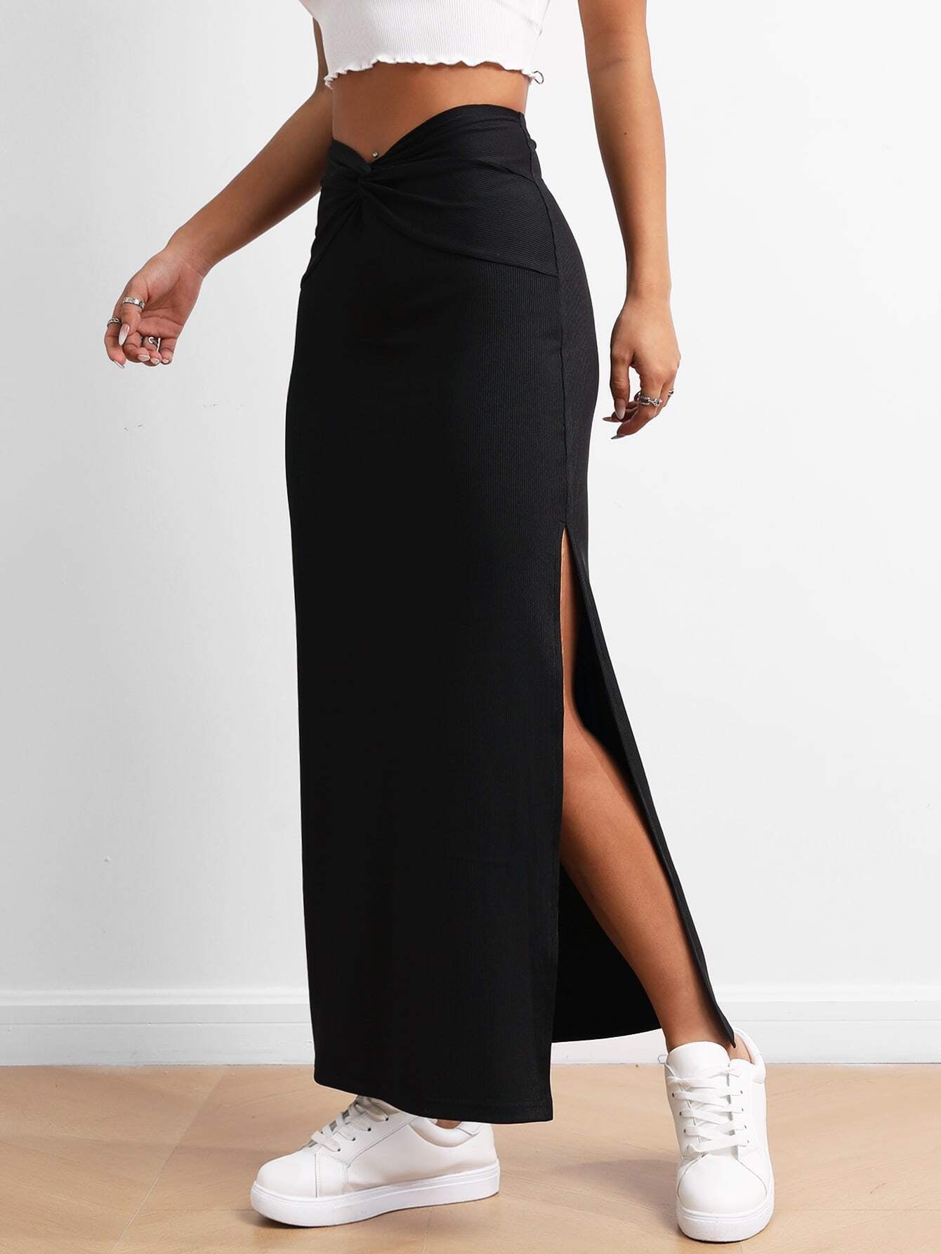 Black long skirt with high side slit and twisted waistband, worn with white sneakers, highlighting the skirt's design details