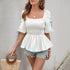 Woman wearing a white peplum blouse with smocked details and embroidered puff sleeves, accessorized with gold jewelry.