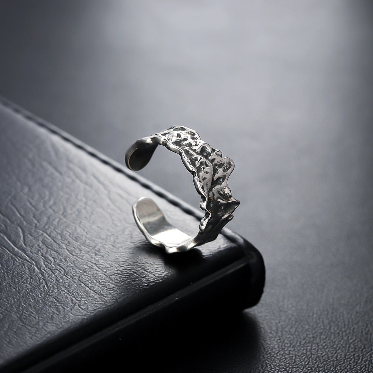 A silver adjustable ring with a hammered texture resting on a black leather surface, reflecting light.