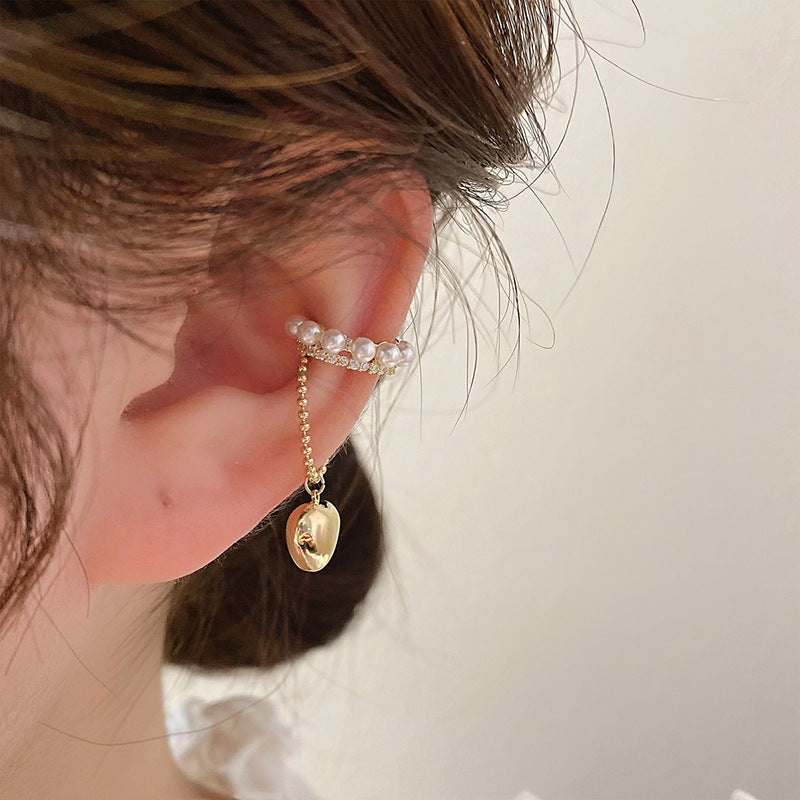 Close-up of pearl and gold ear cuff with heart charm on chain worn on ear