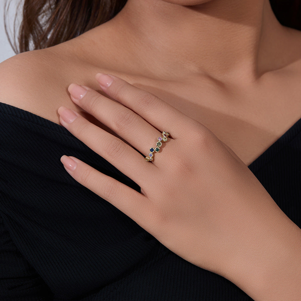 A woman wearing gold rainbow bubble ring on her finger while touching collarbone, dressed in black top