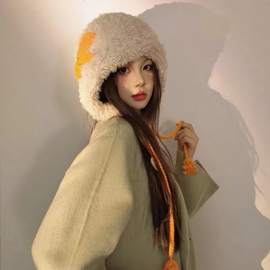 Beige furry winter hat with orange lightning bolt accent and braided ties, paired with sage outerwear