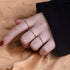Model wearing three dainty gold rings with different colored stones on hand against beige fabric