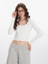 White long-sleeve crop top with scoop neckline and fitted design, shown worn with light gray wide-leg pants with pockets
