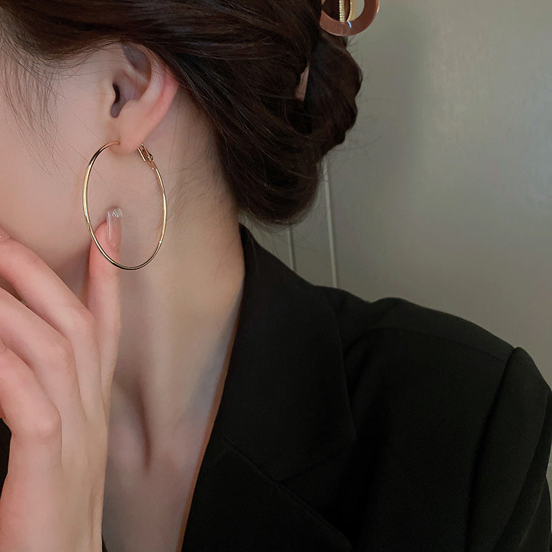 Close-up of woman wearing large gold hoop earring with thin design, shown with dark hair and black blazer