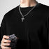 Man wearing a silver cross pendant necklace, holding a glass of ice while dressed in a black sweater