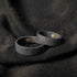 A close-up of two black rings with a hidden gold detail inside, set against black fabric.