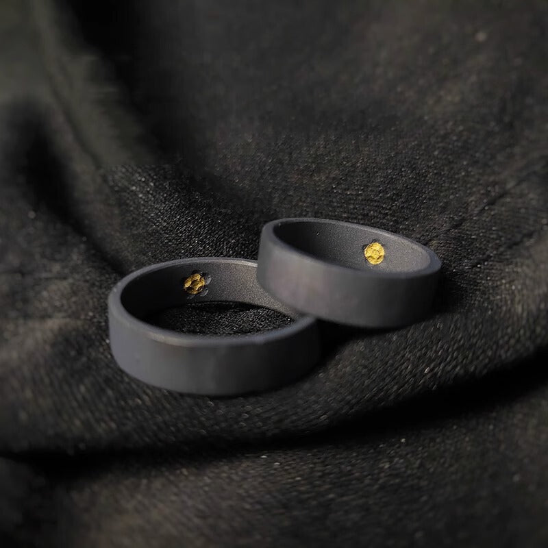 A close-up of two black rings with a hidden gold detail inside, set against black fabric.
