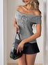 Woman in a gray off-shoulder sweater top with a lace-up detail, styled with a black mini skirt and glossy black handbag.