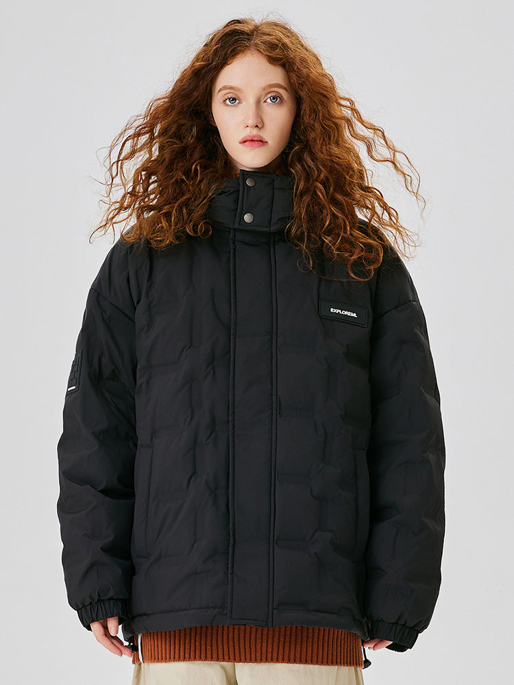 A woman with curly red hair wearing a black puffer jacket with EXPLORERA logo patch, posing against white backdrop