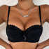 A woman wearing a black lace-trimmed push-up bra with bow detail and silver chain pendant necklace, photographed against white textured background