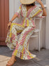 Woman sitting in a boho jumpsuit with a straw hat, featuring a deep V-neck, floral patchwork, and flowy wide-leg pants.