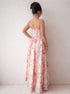 Woman wearing a floral dress standing against a white curtain and wall.