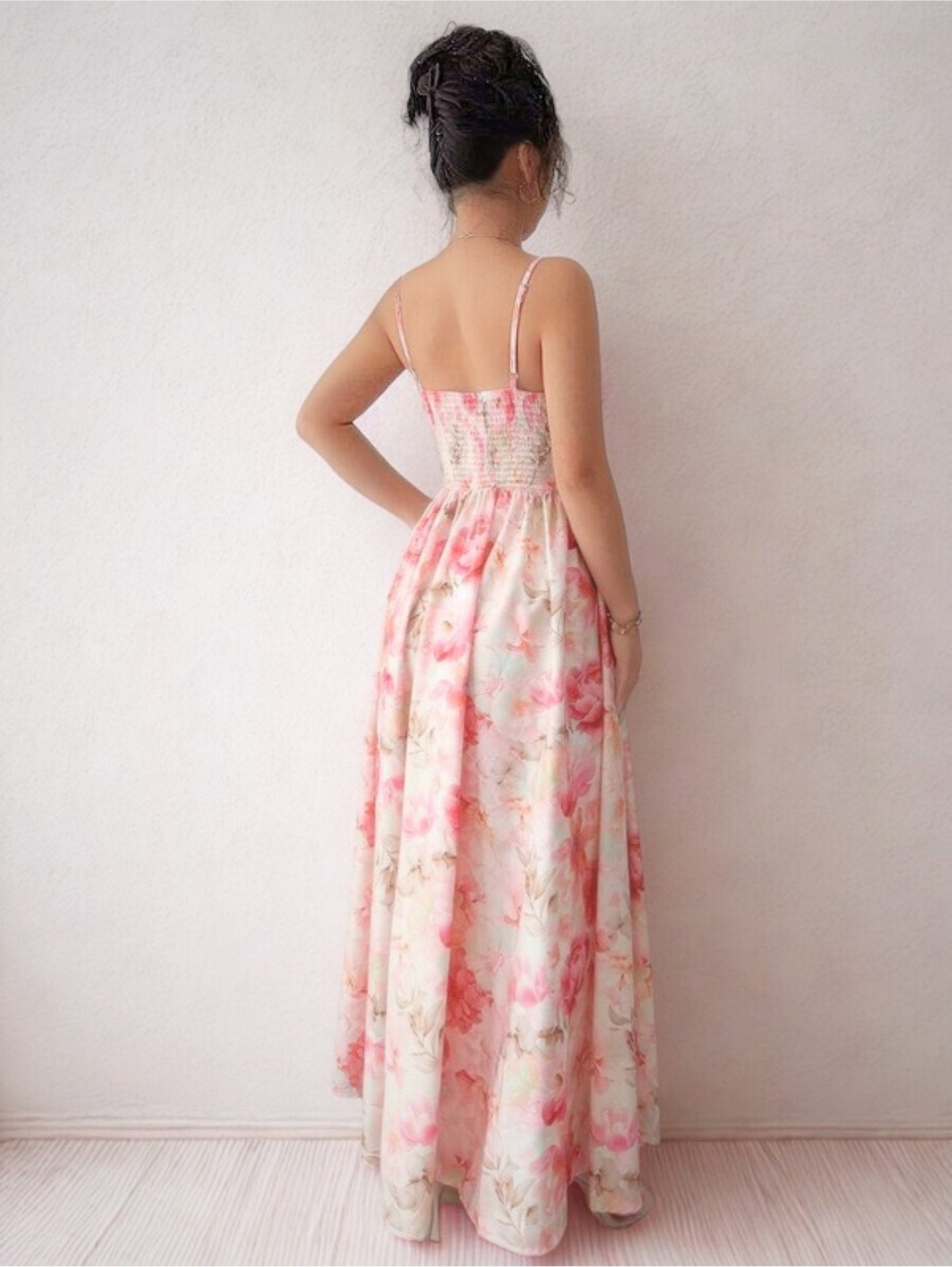 Woman wearing a floral dress standing against a white curtain and wall.