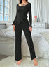 Full-length view of black ribbed jumpsuit with criss-cross detail and ruffle hem pants, styled against white bedroom setting