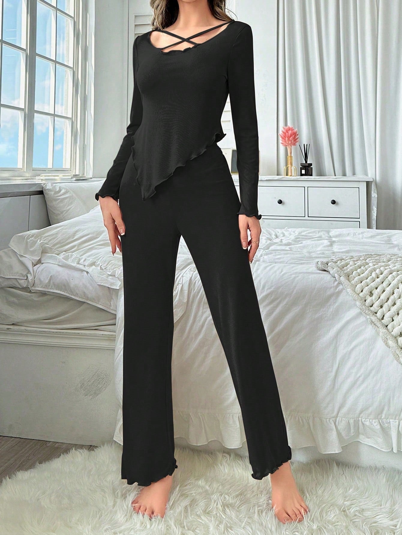 Full-length view of black ribbed jumpsuit with criss-cross detail and ruffle hem pants, styled against white bedroom setting