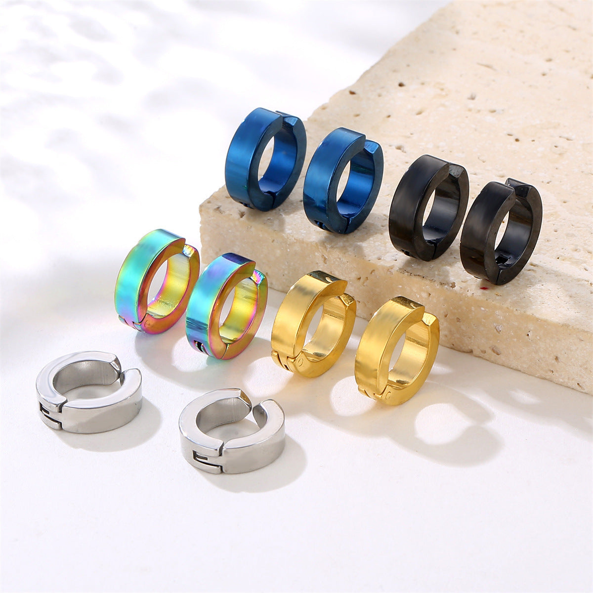 Collection of huggie earrings in various finishes including blue, iridescent, gold, black and silver on stone display