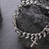 Chunky silver chain bracelet with cross charms displayed on textured black stone for a bold aesthetic.