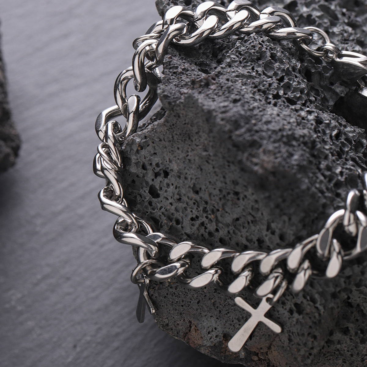 Chunky silver chain bracelet with cross charms displayed on textured black stone for a bold aesthetic.