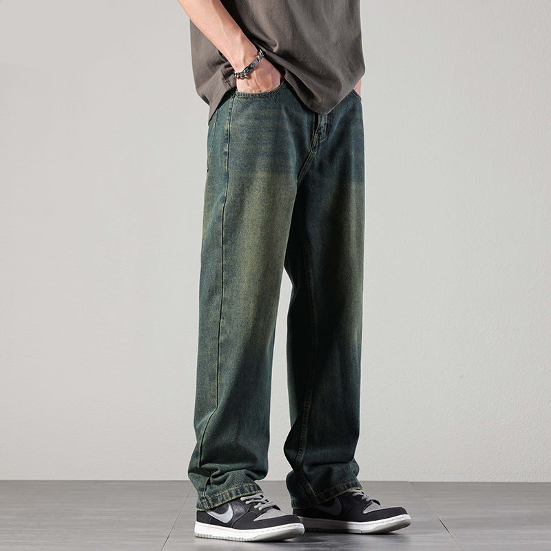 A man in vintage-style loose-fit jeans with a faded wash, a casual t-shirt, and sneakers, standing with one hand in his pocket