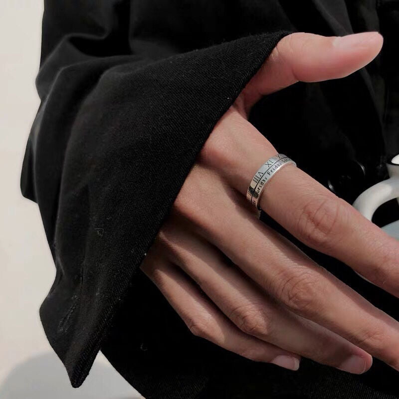 Hand with delicate fingers wearing silver Roman numeral ring with weekday engravings, styled with black fabric for contrast