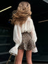 Back view of woman with flowing hair wearing leopard print shorts and a white blouse.