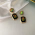 Gold drop earrings featuring iridescent green and gold cabochons displayed on white satin showing unique color-changing effect
