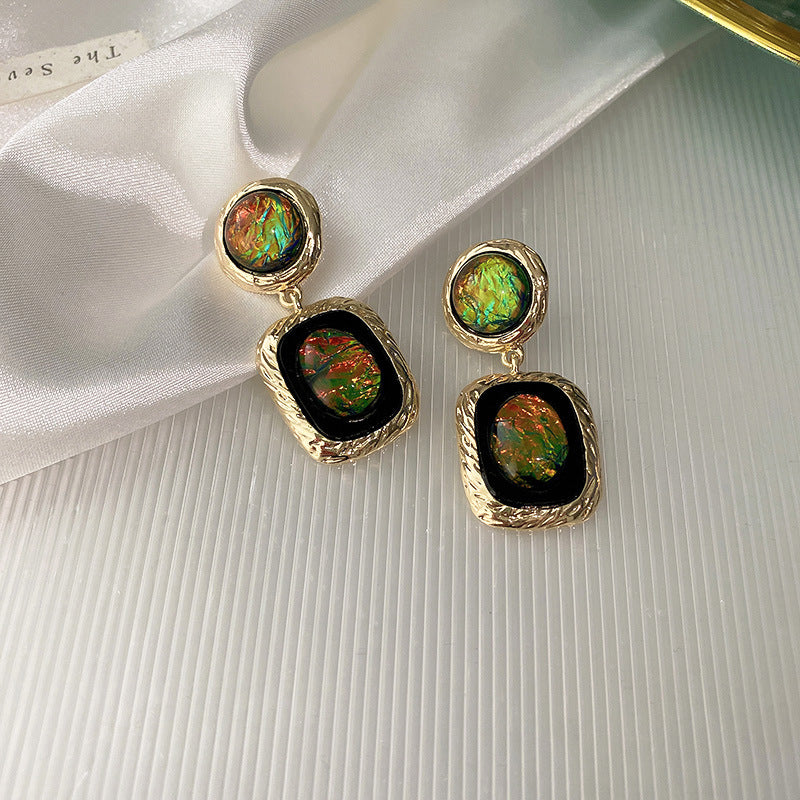 Gold drop earrings featuring iridescent green and gold cabochons displayed on white satin showing unique color-changing effect