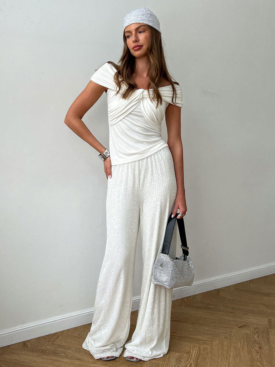 Woman in a white twisted off-shoulder top and sequined pants, holding a silver bag and wearing a silver headscarf