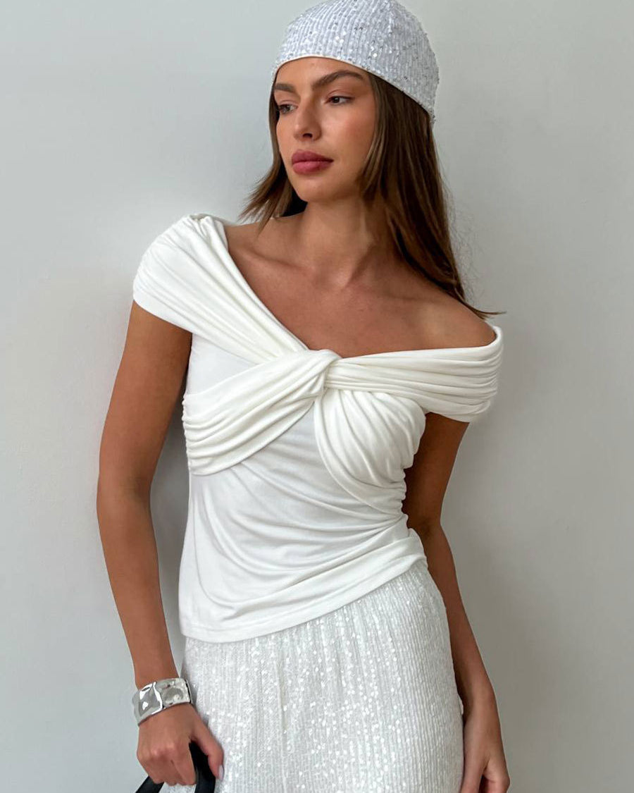 Close-up of a woman in a white off-shoulder twisted top with draped details, wearing a silver headscarf and cuff bracelet