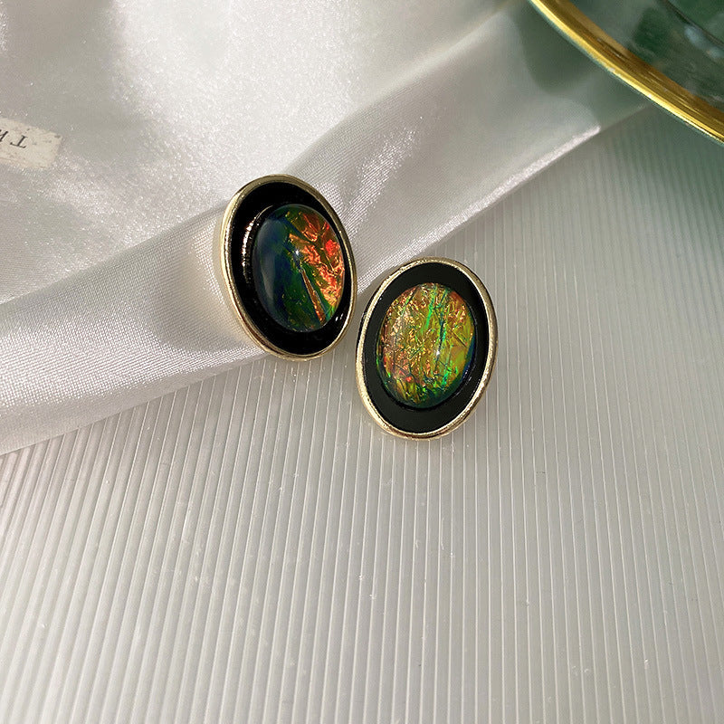 Close-up of oval iridescent green stud earrings with gold rim settings displayed on textured white background showing detailed craftsmanship