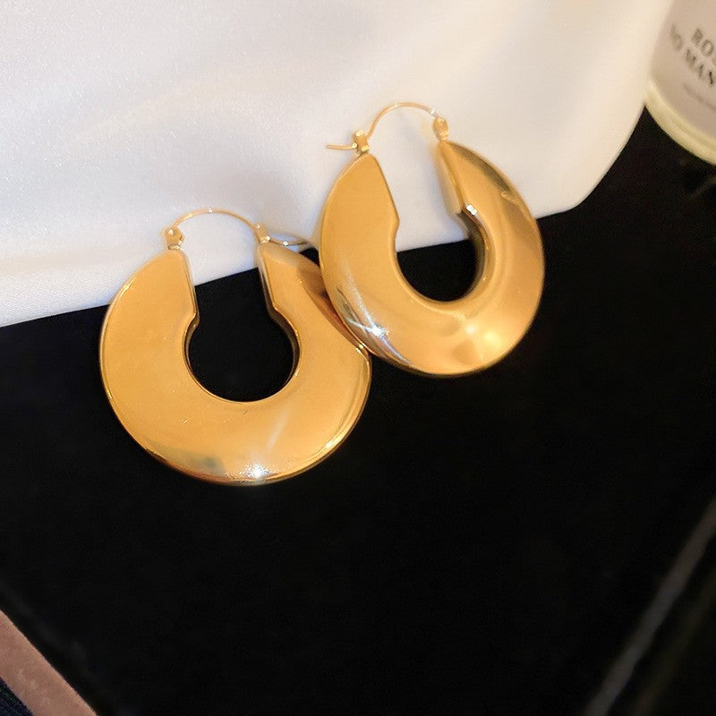 Bold Gold U-Shaped Hoop Earrings – Modern gold hoop earrings with a chunky, crescent-shaped design, placed on a black background