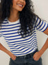 Smiling woman in blue and white striped tee, curly hair, wearing denim