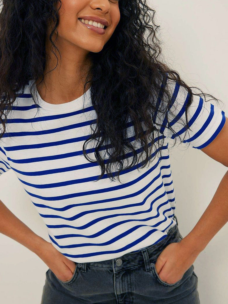 Smiling woman in blue and white striped tee, curly hair, wearing denim