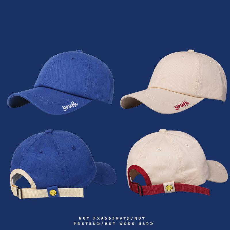Four baseball caps showing front and back views of blue and cream styles with smiley face strap details