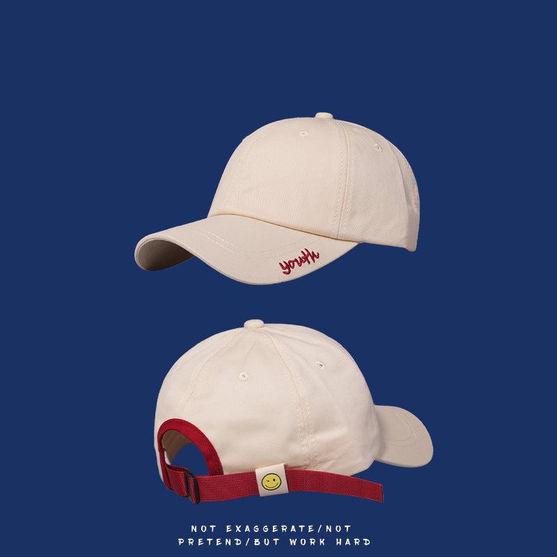 Cream baseball cap with red "youth" embroidery and red adjustable strap with smiley face detail on navy background
