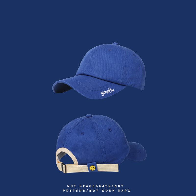 Blue baseball cap front and back views with cream adjustable strap featuring smiley face button on navy background