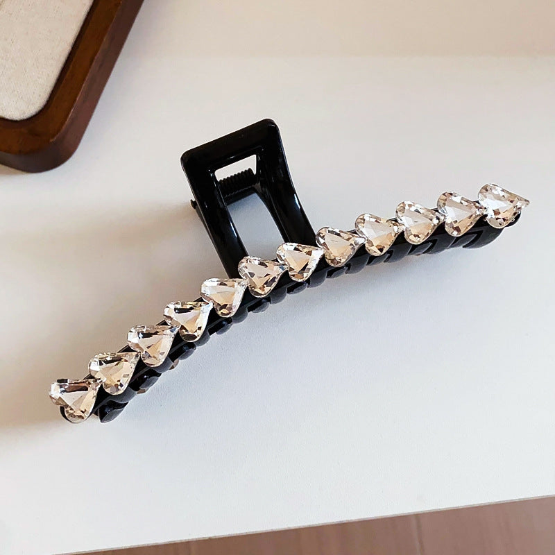 A sleek black hair clip adorned with a row of sparkling heart-shaped crystals, placed on a white surface.