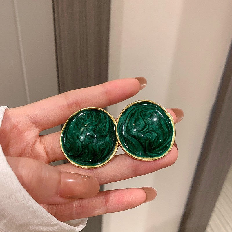 Large circular marbled green earrings with gold settings held in hand showing statement size and unique swirled pattern effect