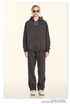 Model wearing charcoal hoodie and sweatpants with silver sunglasses and white sneakers on cream backdrop
