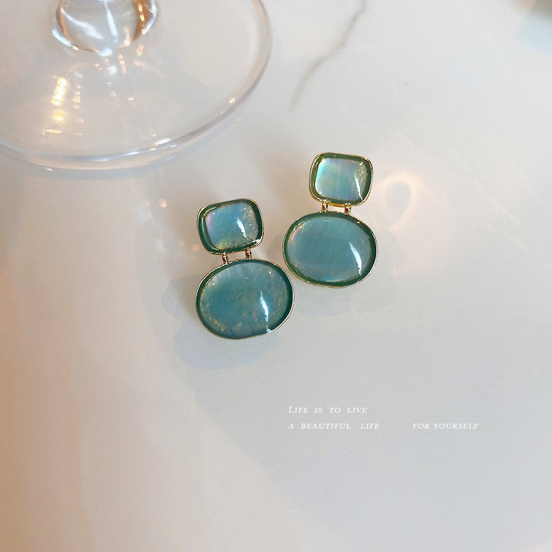 Pale blue-green geometric drop earrings with gold settings displayed on marble surface with inspirational text showing delicate design
