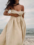 A model is wearing a natural beige linen tie-shoulder dress with gathered waist, standing at the beach with ocean backdrop