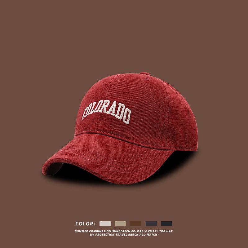 Burgundy red baseball cap with white COLORADO embroidery displayed against brown background with color options shown below