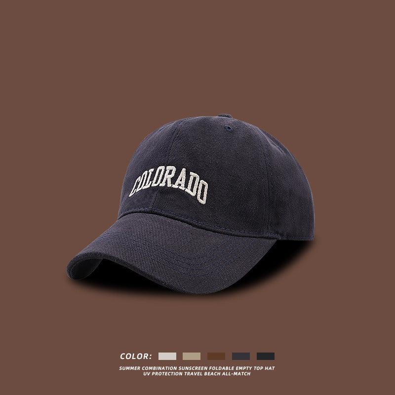 Navy blue baseball cap with white embroidered COLORADO text displayed against brown background, with color options shown at bottom