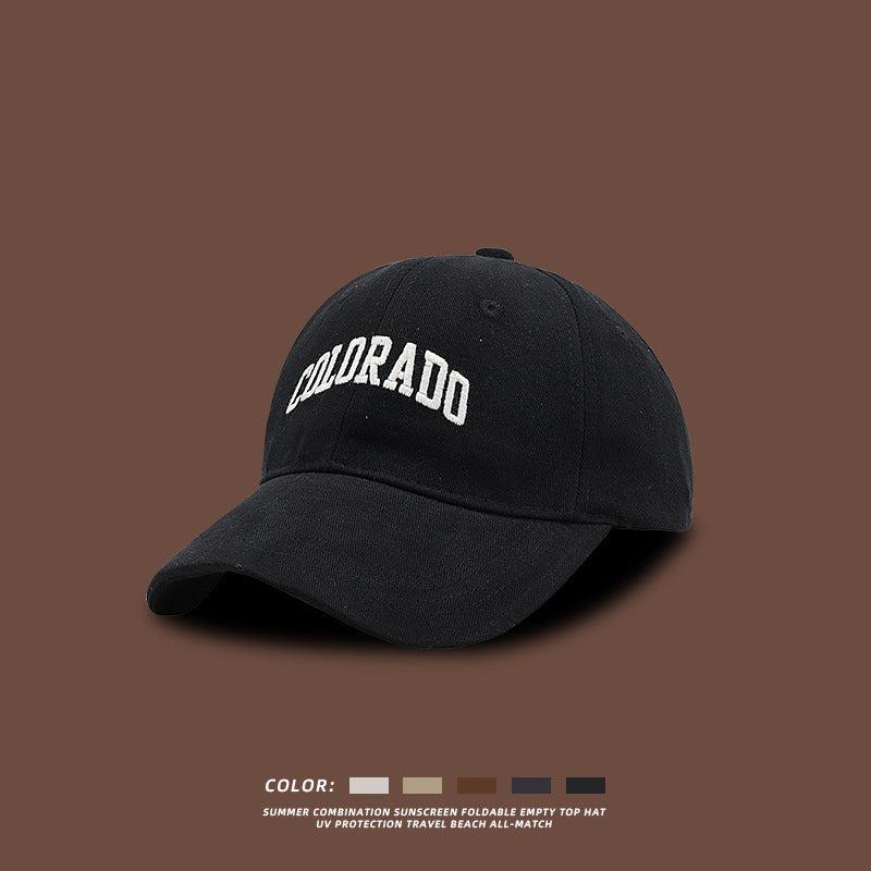 Black baseball cap with white embroidered COLORADO text photographed against brown background with color selection options below