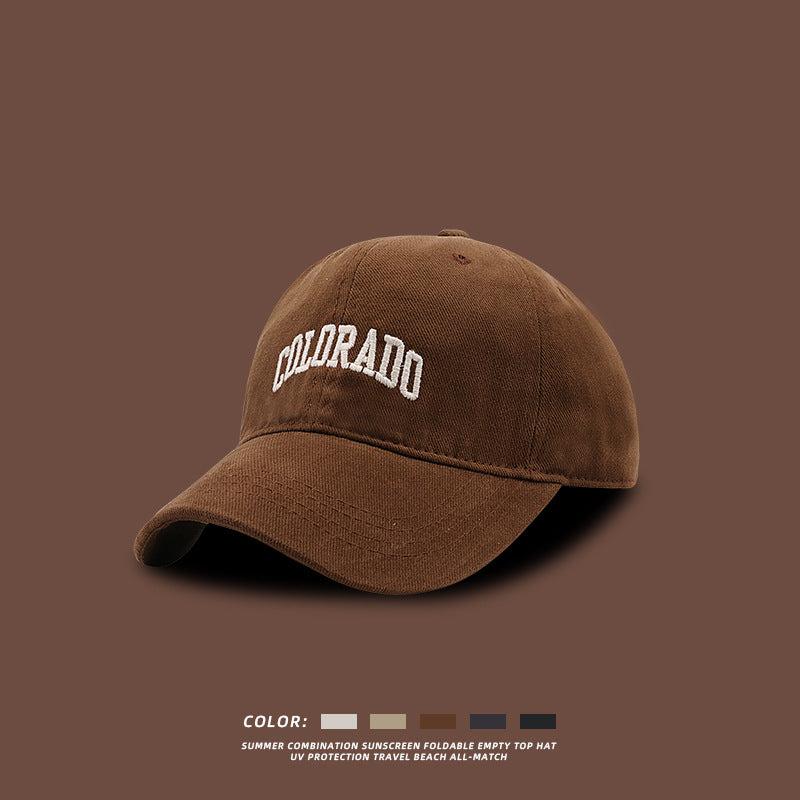 Brown baseball cap with white COLORADO embroidery displayed against matching brown background with color selection swatches below
