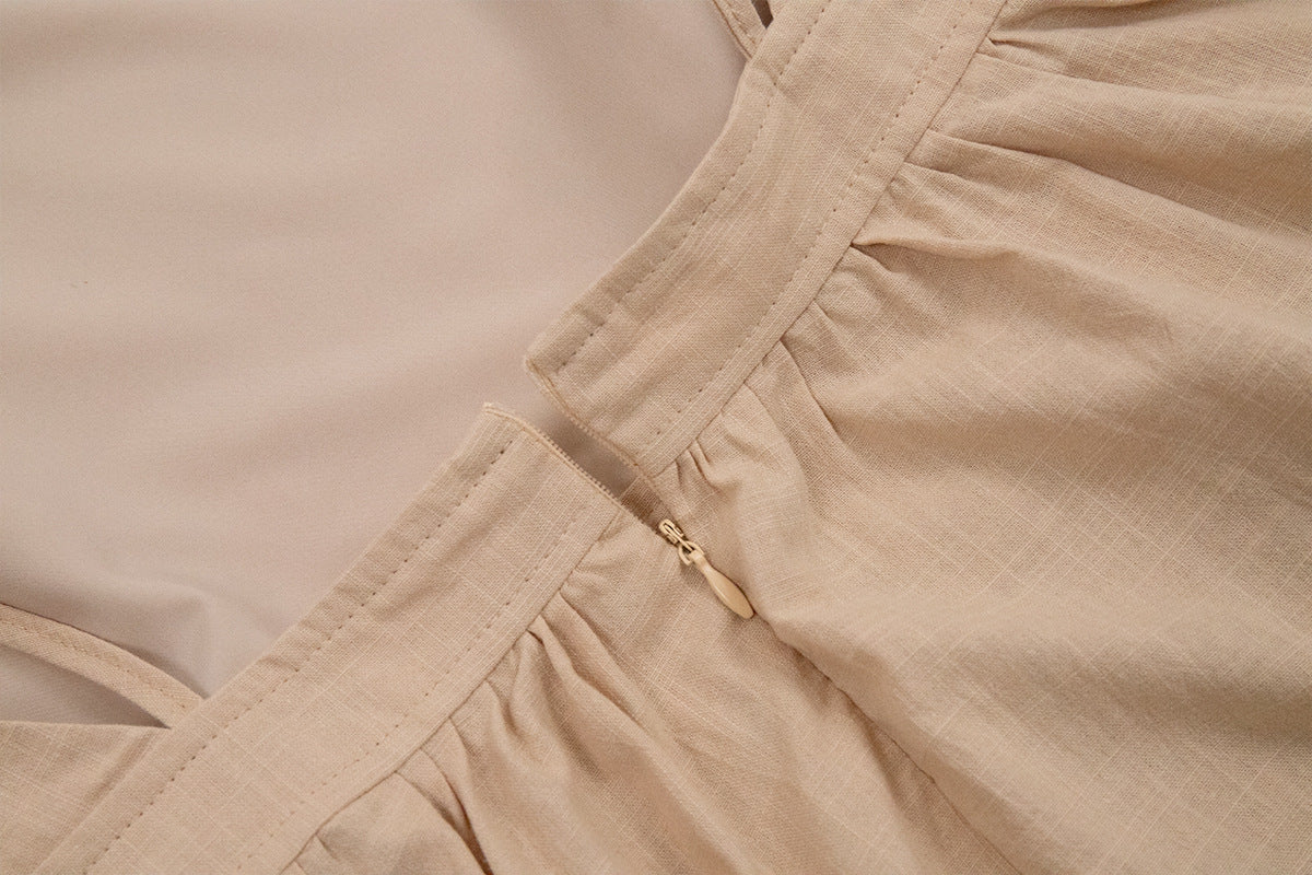 Close-up of beige linen dress showing zipper closure detail and gathered waistband against neutral background