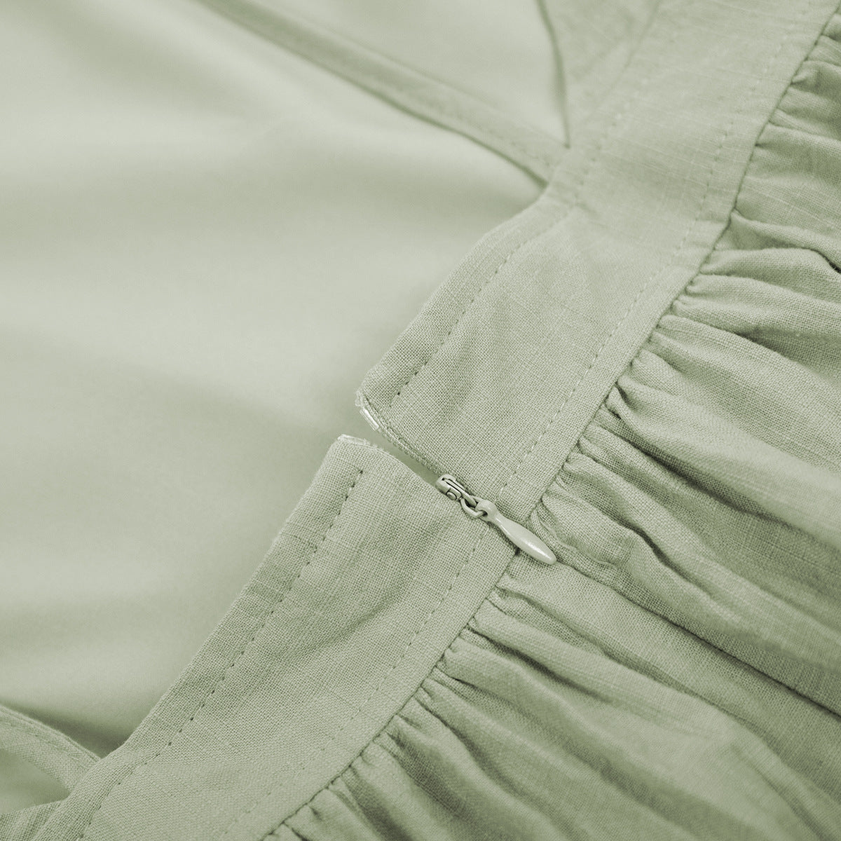 Close-up detail of sage green linen dress showing zipper closure and gathered waistband stitching