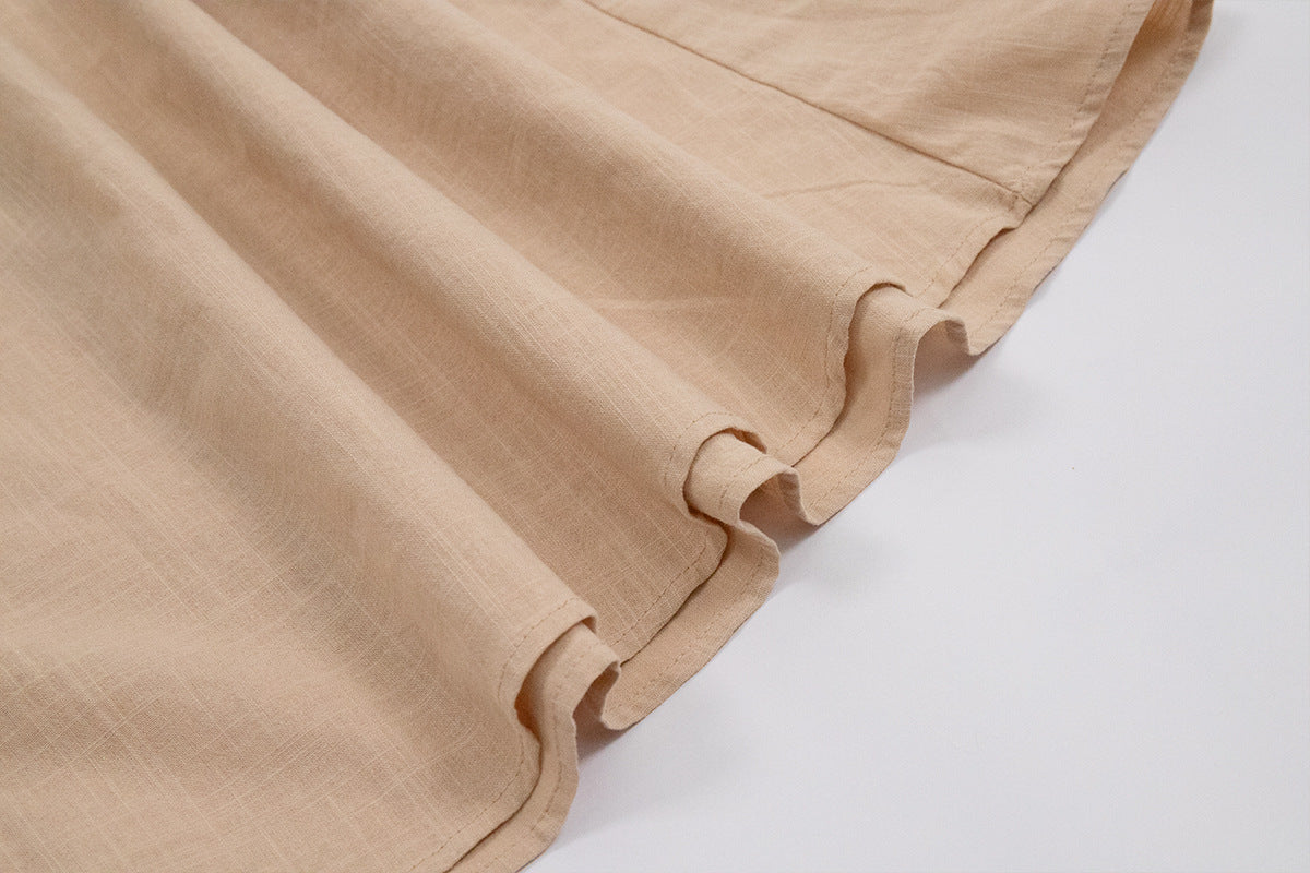 Close-up of beige linen fabric showing gathered hemline detail and stitching against white background